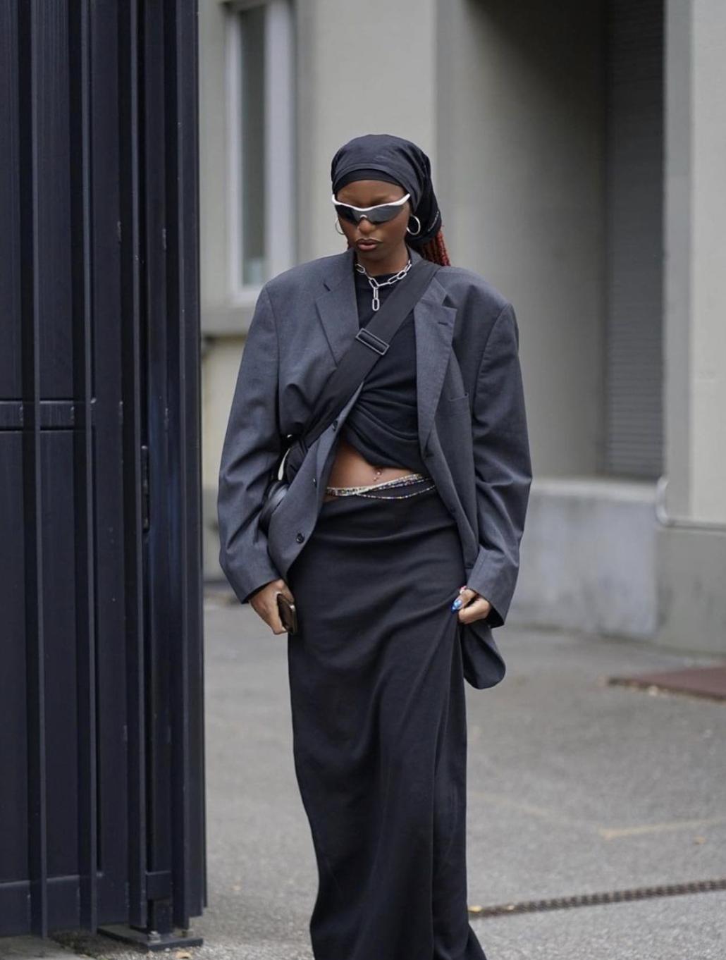 woman in a grey blazer and black bottoms with sunglasses on walking down the street